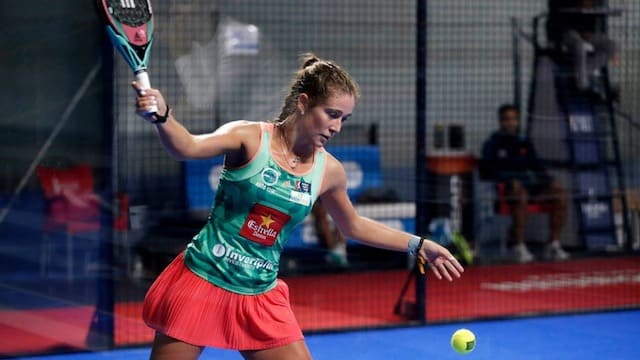 Mujer preparándose para golpear la pelota en su saque de pádel.