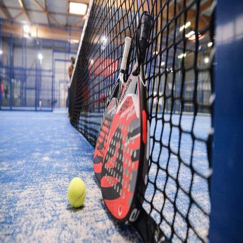 Two padel rackets and a ball leaning towards a net on a padel court.